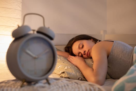 The girl sleeps with her head on a large pillow. The light of a lamp on the wall.