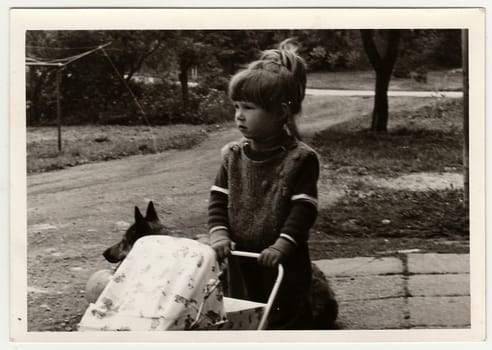 THE CZECHOSLOVAK SOCIALIST REPUBLIC - CIRCA 1970s: Retro photo shows child, girl who plays with toy - dolls pram. Black and white vintage photography.