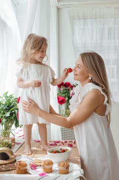 A little blonde girl with her mom on a kitchen countertop decorated with peonies. The concept of the relationship between mother and daughter. Spring atmosphere