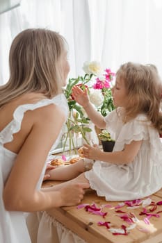 A little blonde girl with her mom on a kitchen countertop decorated with peonies. The concept of the relationship between mother and daughter. Spring atmosphere