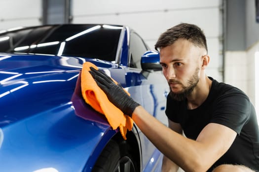 Hand car drying with microfiber in detailing auto service. Cleaner worker dry body car after washing automobile