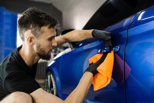 Hand car drying with microfiber in detailing auto service. Cleaner worker dry body car after washing automobile