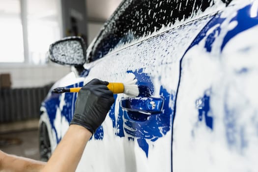 Hand brush washing of car body with foam in car detailing service. Car wash worker washes a car body