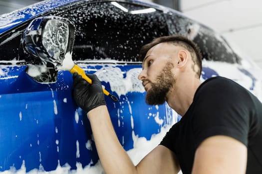 Hand brush washing of car side mirror with foam in car detailing service. Car wash worker washes auto body