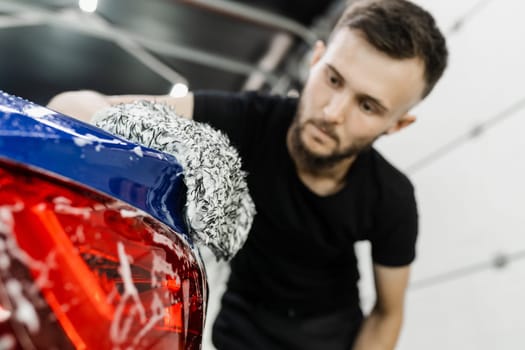 Car washer doing manual foam washing in auto detailing service. Hand washing with microfiber glove with foam car body in garage