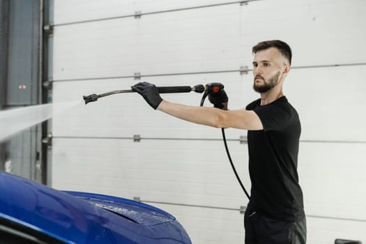 Spraying water on car to wash off foam in the garage. Process of detailing washing in car service. Car washer pouring water for full body car wash