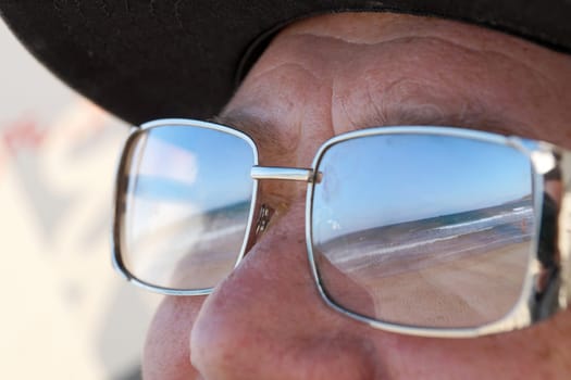 the beach and the sea are reflected in the man's sunglasses close-up