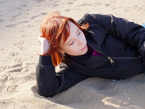 portrait of a red-haired teenage girl lying on the sand.