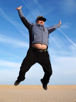 adult man jumping with his arms outstretched against the sky.