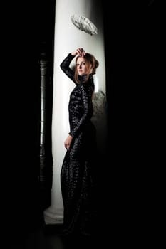 Attractive woman posing in black cocktail dress near column