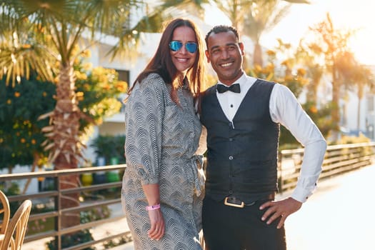 Mature woman standing with waiter that in official clothes.