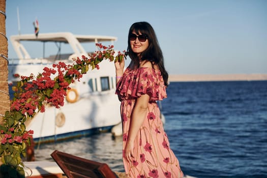 Cheerful mature woman standing against white yacht on the sea.