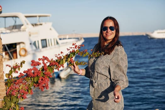 Cheerful mature woman standing against white yacht on the sea.