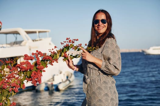 Cheerful mature woman standing against white yacht on the sea.