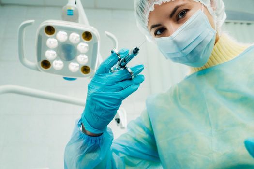 A masked dentist holds an injection syringe for a patient in the office.