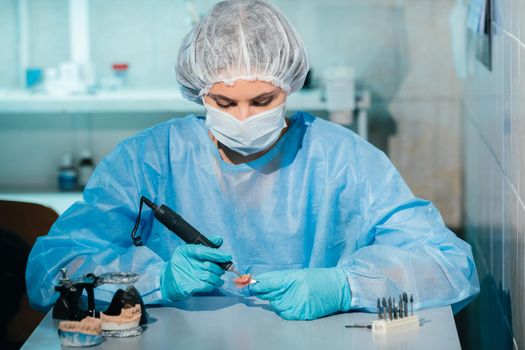 A masked and gloved dental technician works on a prosthetic tooth in his lab.