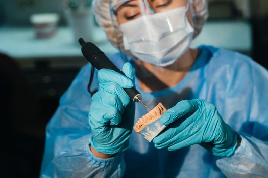 A masked and gloved dental technician works on a prosthetic tooth in his lab.