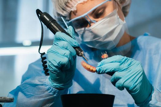 A masked and gloved dental technician works on a prosthetic tooth in his lab.