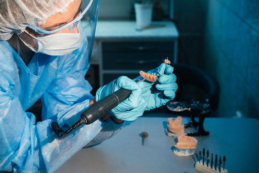 A masked and gloved dental technician works on a prosthetic tooth in his lab.