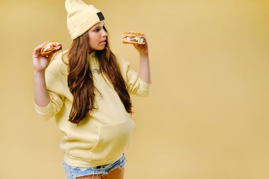 pregnant girl in yellow clothes with hamburgers in her hands on a yellow background.
