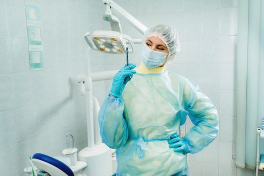 A masked dentist holds an injection syringe for a patient in the office.