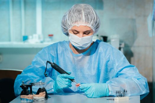 A masked and gloved dental technician works on a prosthetic tooth in his lab.