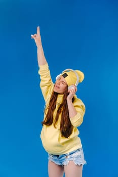 A pregnant girl in a yellow jacket and headphones stands on a blue background.