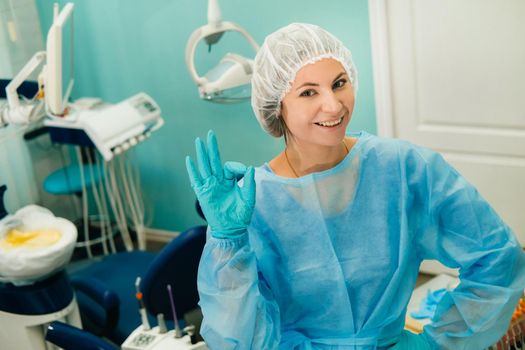 the dentist stands in his office and shows the OK sign.