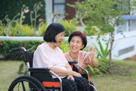 Daughter caring for the elderly asian woman ,do selfie, happy, smiles in backyard.