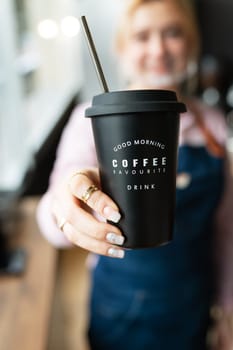 Barista girl holding a black metal glass with the inscription good morning favorite coffee drink in her hands with prepared hot coffee. Professional coffee preparation