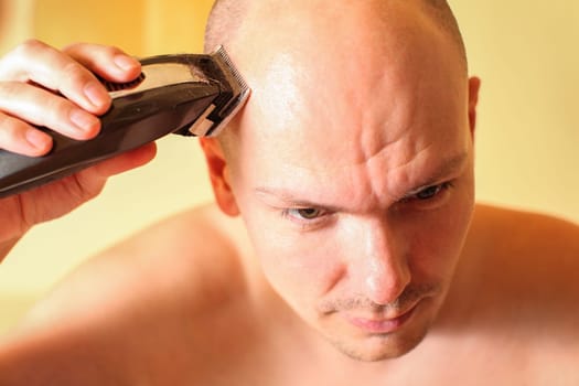 Young man shaving his head with electric haircutter.