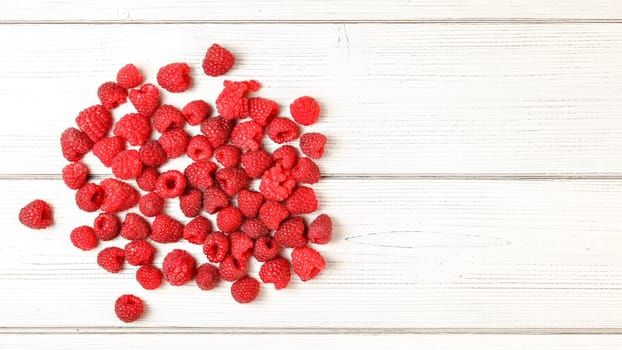 Tabletop view, pile of freshly picked raspberries spilled on white boards desk. Space for text on the right.