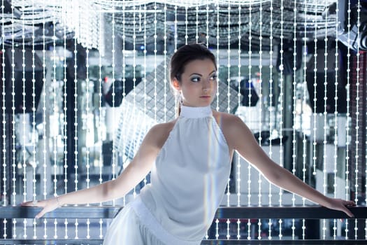 Glamour portrait of young woman in long white dress posing in night club