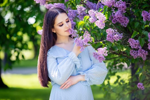 Pretty girl with long hair , in light blue dress stands with lilac flowers, in the garden, in sunny day. Close up. copy space
