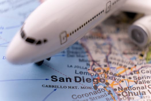 Close up detail of a miniature passenger airplane on a colorful map focusing on San Diego, California through selective focus, background blur.