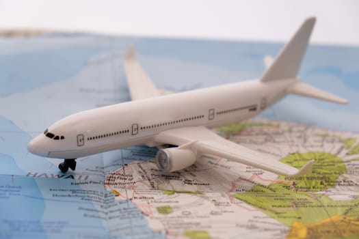 Close up detail of a miniature passenger airplane on a colorful map focusing on Hawaii through selective focus, background blur.
