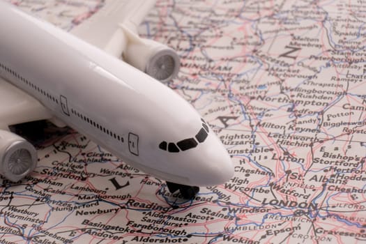 Close up detail of a miniature passenger airplane on a colorful map focusing on London England through selective focus, background blur.