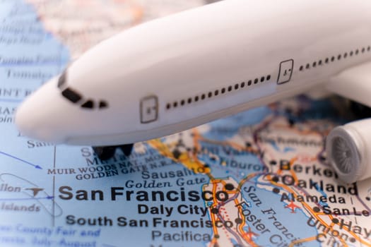 Close up of a miniature passenger airplane on a colorful map focusing on San Francisco, California through selective focus, background blur.