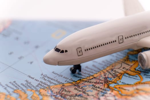 Close up detail of a miniature passenger airplane on a colorful map focusing on Amsterdam, Netherlands through selective focus, background blur.