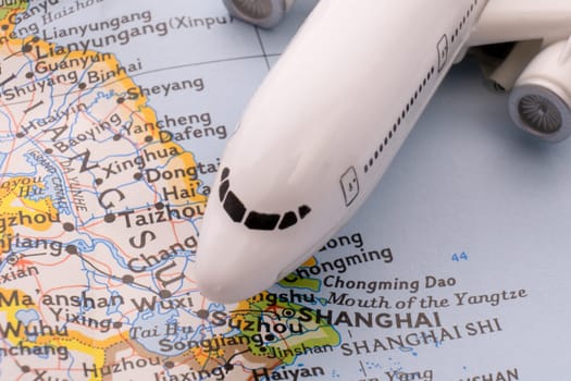 Close up detail of a miniature passenger airplane on a colorful map focusing on Shanghai, China through selective focus, background blur.