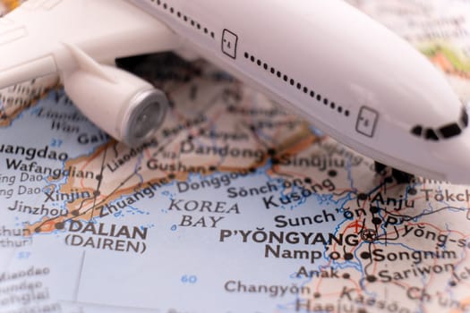 Close up detail of a miniature passenger airplane on a colorful map focusing on Pyongyang North Korea through selective focus, background blur.