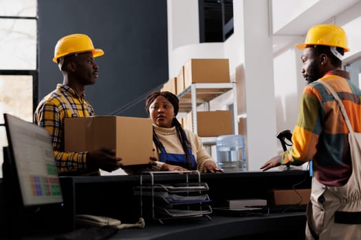 Postal service workers bringing received parcel for registration at reception desk. African american shipment operators managing package dispatching in delivery company warehouse