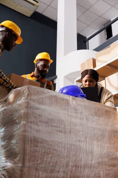 Warehouse workers managing packages sorting and dispatching on laptop. African american delivery service company employees preparing parcels for shipment in postal storehouse