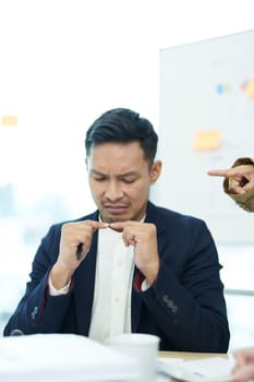 An image of an Asian male employee looking worried and sad about being scolded by his boss for failing to meet sales targets, concept of disappointment and failure in his career.