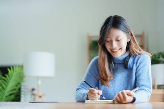 Portrait of a teenage Asian woman using a notebook to study online via video conferencing on a wooden desk at home.