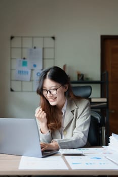 Portrait of a woman business owner showing a happy smiling face as he has successfully invested her business using computers and financial budget documents at work.