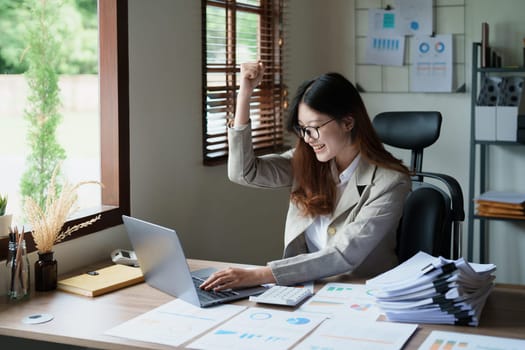 Portrait of a woman business owner showing a happy smiling face as he has successfully invested her business using computers and financial budget documents at work.