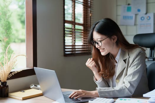 Portrait of a woman business owner showing a happy smiling face as he has successfully invested her business using computers and financial budget documents at work.