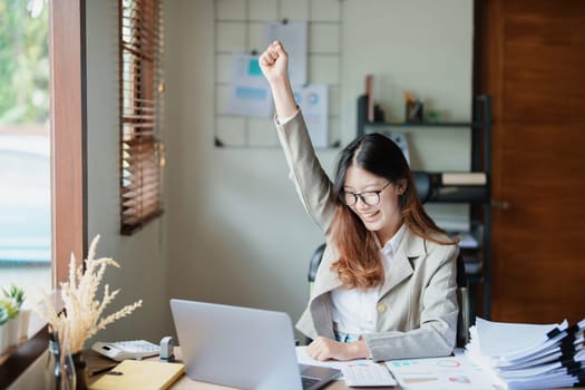 Portrait of a woman business owner showing a happy smiling face as he has successfully invested her business using computers and financial budget documents at work.