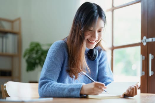 Portrait of a teenage Asian woman using a notebook to study online via video conferencing on a wooden desk at home.